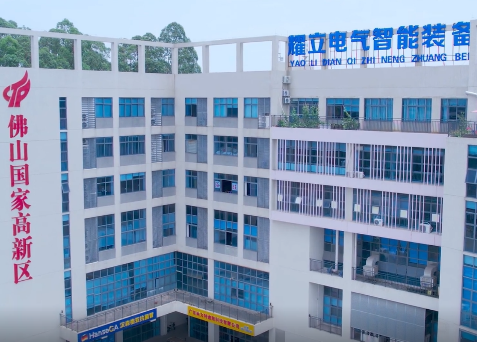 现代化工业厂房外景,灰色建筑配蓝色玻璃幕墙,绿色植物环绕,阳光明媚天气